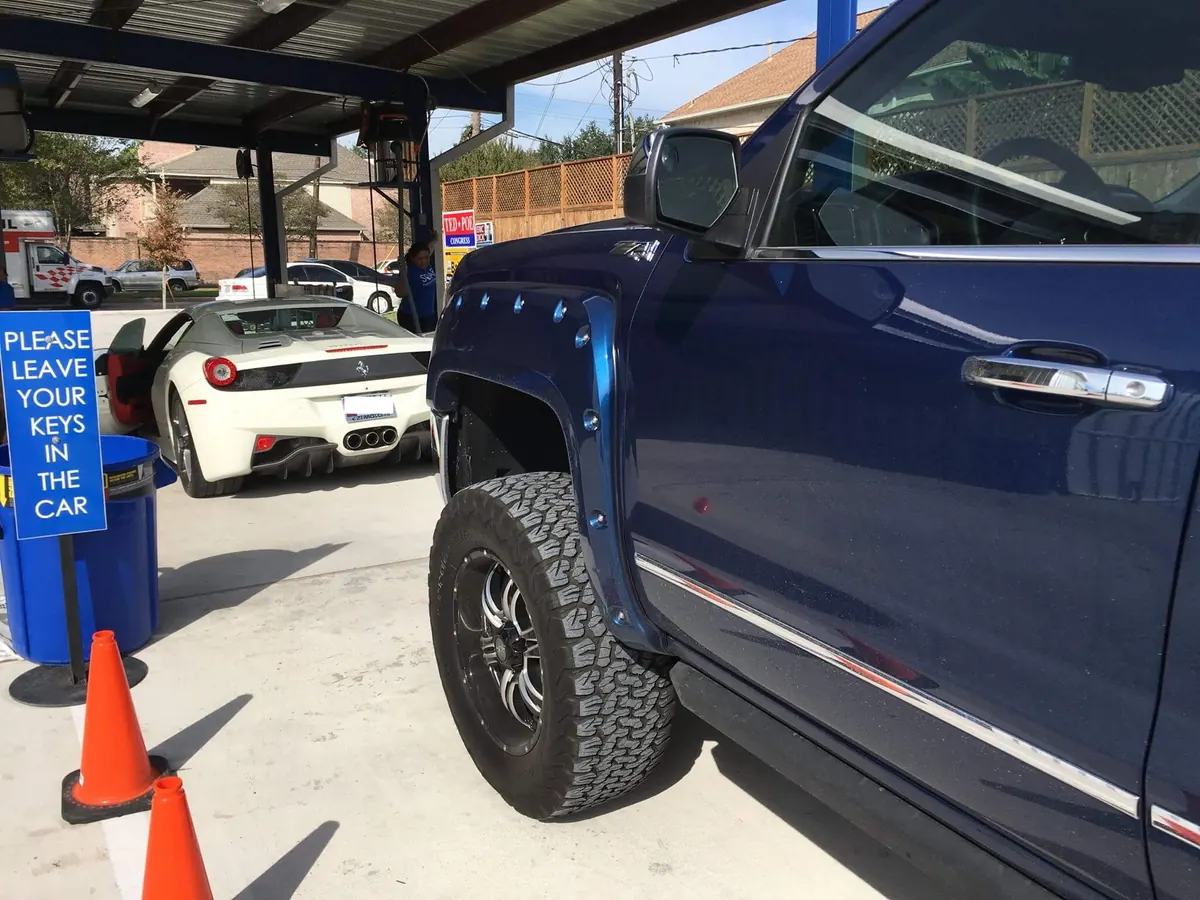 Lifted blue pickup truck and a white Ferrari under the wash canopy at SOAP Hand Car Wash