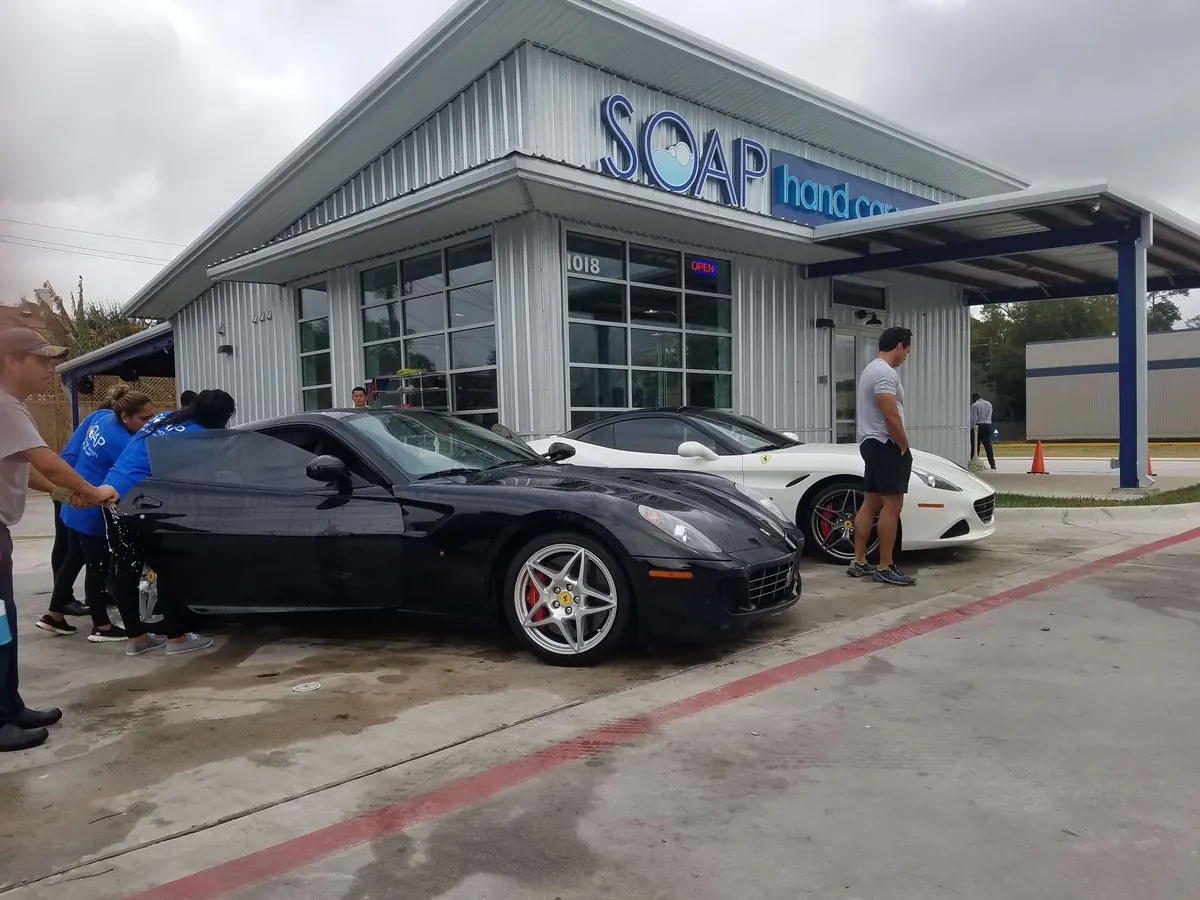 SOAP crew hand washing a black Corvette in front of the store