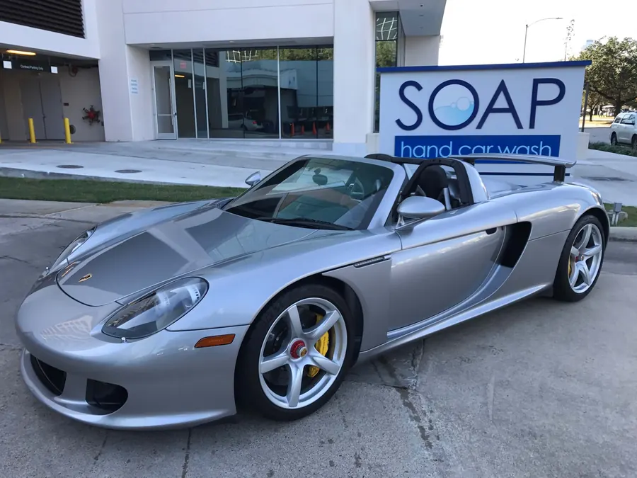 Silver Porsche Carrera GT with a mirror finish parked by the SOAP Hand Car Wash sign